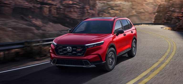 2027 Honda CR-V TrailSport Hybrid in Radiant Red Metallic front driving on a winding mountain road (Compact Crossover SUV). 2027 Honda CR-V TrailSport Hybrid in Radiant Red Metallic front driving on a winding mountain road (Compact Crossover SUV).
