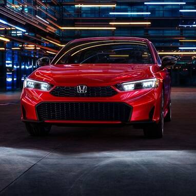 2027 Honda Civic Sedan Sport Touring Hybrid in Rallye Red front view with headlights on (Compact Sedan)